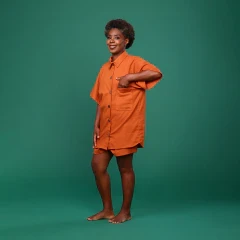 Imagem de modelo com manequim 38, altura de 1,55 e peso de 52 kg, usando o tamanho P de uma camisa oversized em linho na cor terracota. A peça apresenta bolso lateral, botões de casca de coco